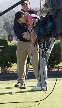 Young woman golfer putting, with Bill Cole and camera equipment